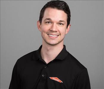 Male SERVPRO Technician with brown hair smiling in front of a gray background